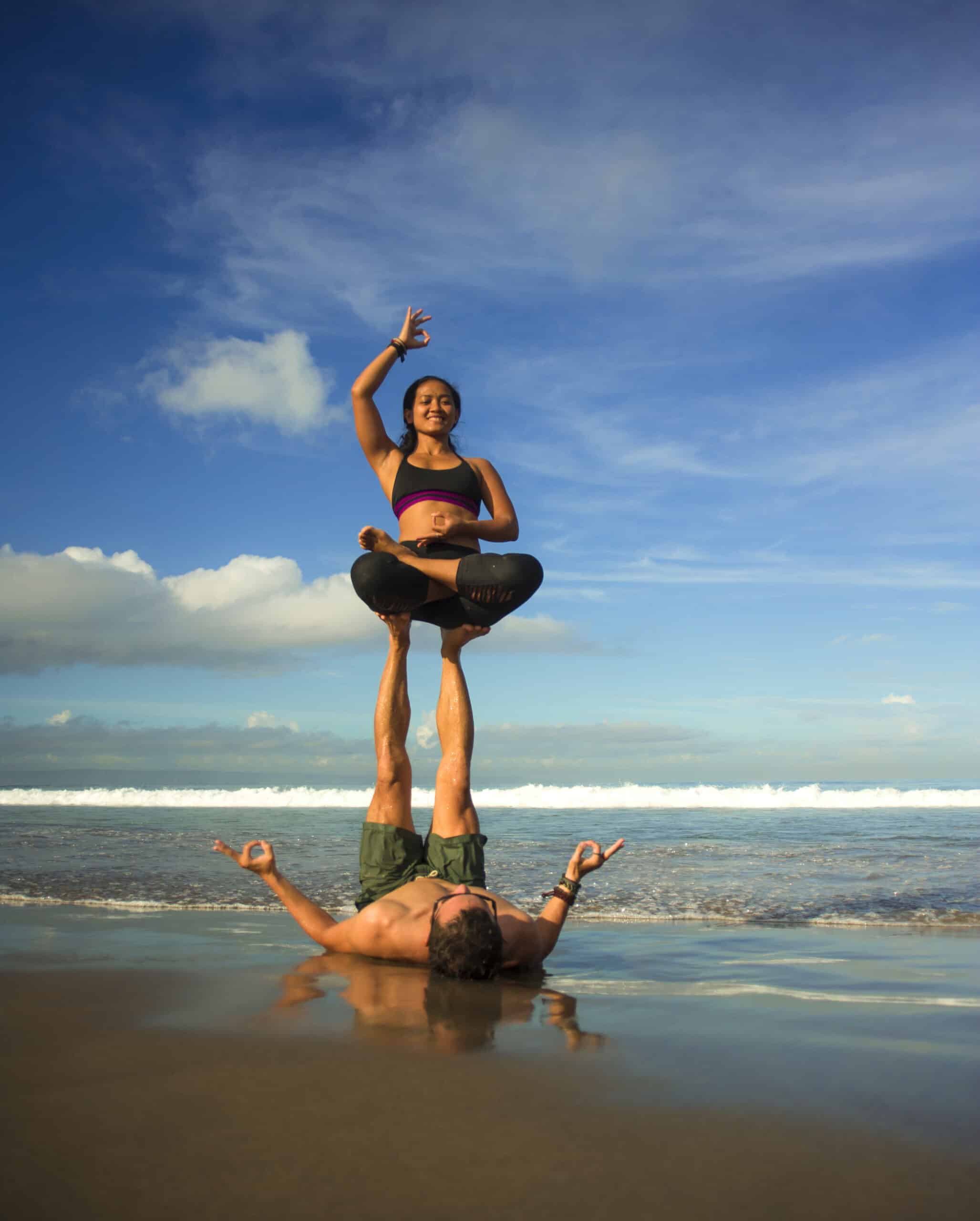 young attractive and concentrated couple of acrobats practicing acro yoga balance and meditation exercise on beautiful beach under a blue sky in mind and body control